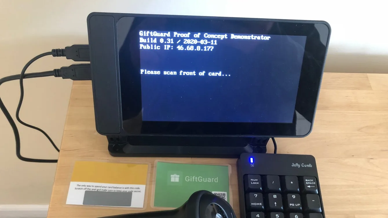 The GiftGuard proof-of-concept demonstrator on a desk: a small screen prompting “Please scan front of card…”, with a barcode scanner, a numeric keypad and two sample gift cards