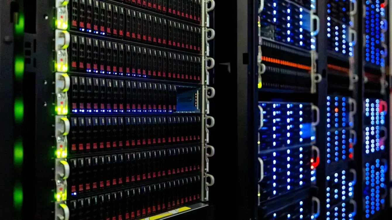 Rows of rack-mounted servers in a darkened server room, their status lights lit green, blue and red