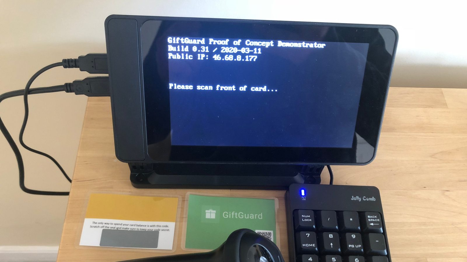 The GiftGuard proof-of-concept demonstrator on a desk: a small screen prompting “Please scan front of card…”, with a barcode scanner, a numeric keypad and two sample gift cards